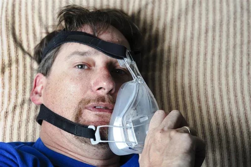 man wearing a CPAP mask, exhausted, sitting up in bed