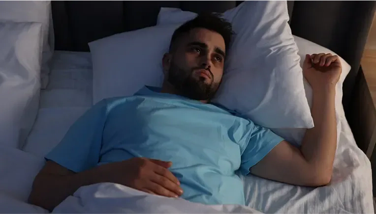 man awake at night, checking phone, exhausted